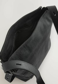 Borsa a mano in pelle nera con una texture morbida, apertura superiore e tracolla regolabile. L'interno presenta un unico scomparto per lo stoccaggio.