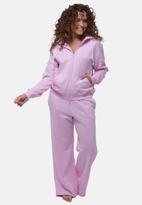 Roze fleece trainingspak met ritscapuchon en trekkoord. Voorzien van zijzakken en relaxte pasvorm bij de broek. Zachte textuur en casual ontwerp.