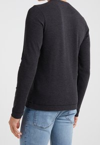 Long-sleeve, dark grey fitted top made of textured fabric, with a round neck and wrist cuffs, paired with light blue denim jeans.