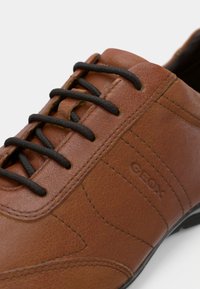 Chaussure en cuir marron avec lacets noirs, coutures détaillées, et "GEOX" embossé sur le côté près des lacets.