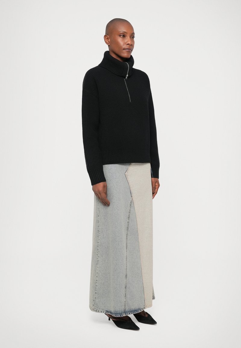 Svart stickad tröja med hög krage och en kort dragkedja, i kombination med en lång denimbakelsekjol i grått och beige.