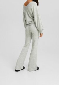 Maglione grigio lavorato a maglia con maniche ampie e scollatura a V, abbinato a pantaloni a zampa coordinati, entrambi con un tessuto testurizzato. Calzature nere.