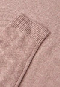 Helle rosa gestrickte Stoff mit einem gerippten Bündchen, der eine glatte Textur und ein einheitliches Muster zeigt. Nahaufnahme des Ärmeldesigns.
