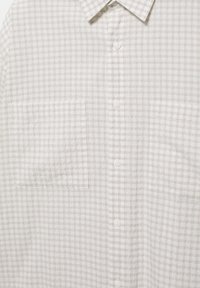 Chemise blanche à boutons avec un motif quadrillé marron clair et deux poches poitrine, vue du col jusqu'au milieu du torse.