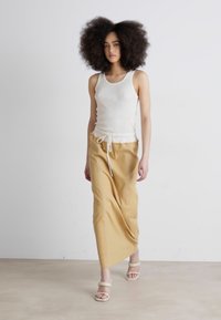 Débardeur léger en crème et longue jupe fluide de couleur beige clair avec une taille élastique et un détail à cordon, associée à des sandales beiges à brides.