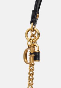 Fermoir en métal doré avec détails en cuir noir, chaîne en or maillée, anneaux circulaires et détail de cadenas décoratif. Finitions de surface texturées visibles.