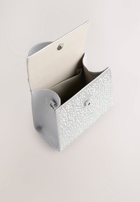 Bolso de mano plateado con superficie texturizada decorada con pequeñas gemas reflectantes; cuenta con cierre de solapa y un interior beige con compartimentos.