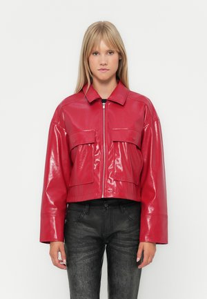 Giacca rossa cropped in pelle lucida con zip frontale, collo oversize e due tasche laterali. Indossata con pantaloni neri testurizzati.