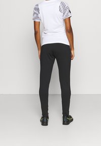 Zwarte getailleerde leggings gecombineerd met een wit shirt met grijze patroonmouwen, ontworpen voor sportief gebruik. Gladde textuur en aansluitende stijl.
