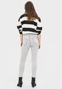 Randig svart och vit tröja med neddragna axlar, ihop med ljusgrå skinny jeans med bakfickor och svarta stövletter som går upp till anklarna.