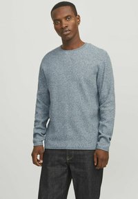 Hellblauer gestrickter Pullover mit langen Ärmeln, rundem Ausschnitt und subtiler Textur. Kombiniert mit dunklen Jeans.