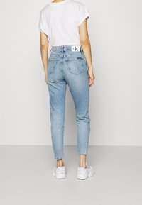 Světle modré džíny s přiléhavým střihem, vysokým pasem a zadními kapsami. Doplněné bílým tričkem a bílými teniskami.