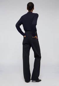 Top de manga larga en navy combinado con pantalones de pierna ancha negros de cintura alta. Textura de tela suave con dos bolsillos traseros y un acabado limpio.