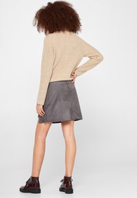 Beige gebreide trui met een ribbelstructuur, gecombineerd met een grijze suede mini-jurk. Het model draagt donkerbruine enkellaarzen met een stevige zool.