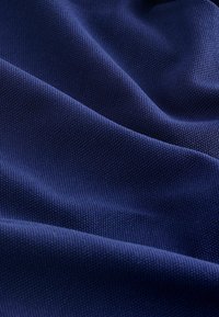 Tengerészkék texturált szövet, szőtt mintával, amely lágy redőzéseket és enyhe fényt mutat, kiemelve sima, tapintható felületét.