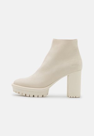 Cremefarbener Leder-Knöchelboot mit klobigem Blockabsatz und Profilsohle, minimalistisches Design und dezentes, geprägtes Branding nahe der Ferse.