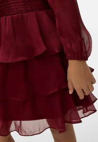 Vestito a strati color bordeaux con tessuto trasparente, dettagli arricciati e maniche lunghe. Presenta un corpetto texturizzato con dettagli raccolti.