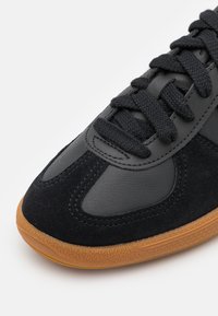 Sneaker nera con tomaia in suede e pelle liscia, lacci testurizzati e suola in gomma naturale. Presenta un design snello con accenti curvi.