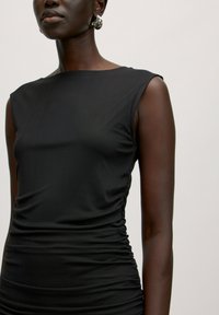 Schwarzes, ärmelloses Kleid mit figurbetonter Passform, das an der Seite eine geraffte Textur und einen glatten, leichten Stoff aufweist.