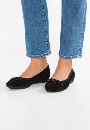 Black suede ballet flats with a rounded toe, featuring a decorative beaded accent on the front, paired with light blue cropped jeans.