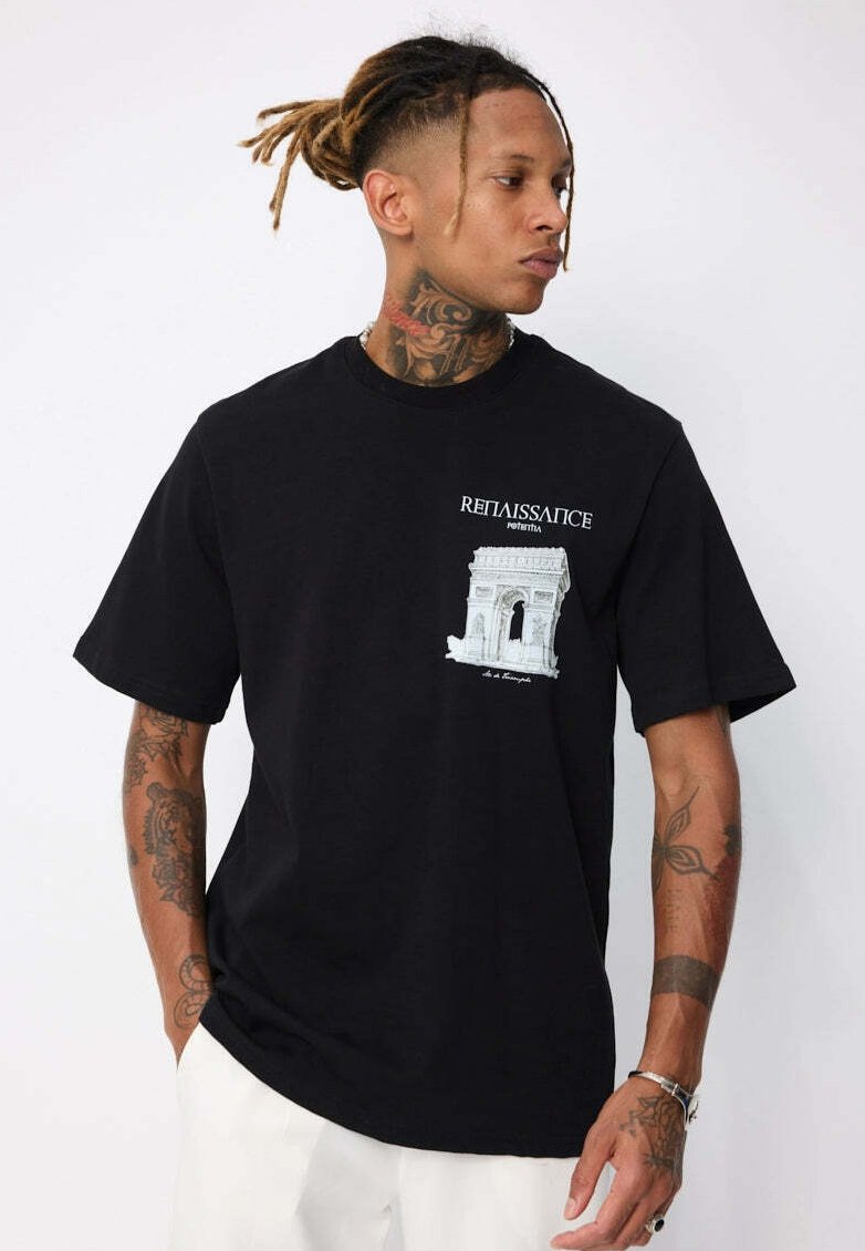 Homme avec des dreadlocks et des tatouages portant un t-shirt noir avec un graphique blanc de l'Arc de Triomphe et le texte "Renaissance Portugal", pantalon blanc.