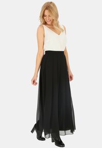 Czarna, plisowana spódnica maxi zestawiona z białym topem bez rękawów, z głębokim dekoltem w kształcie litery V. Spódnica jest zwiewna z przezroczystą nakładką. Czarne botki na obcasie.