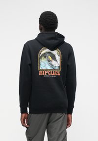Zwarte hoodie met een kleurrijke graphic op de achterkant van een skelet dat surft, met "RIP CURL" en "SHRED TILL DEAD." Gemaakt van katoen, ontspannen pasvorm.