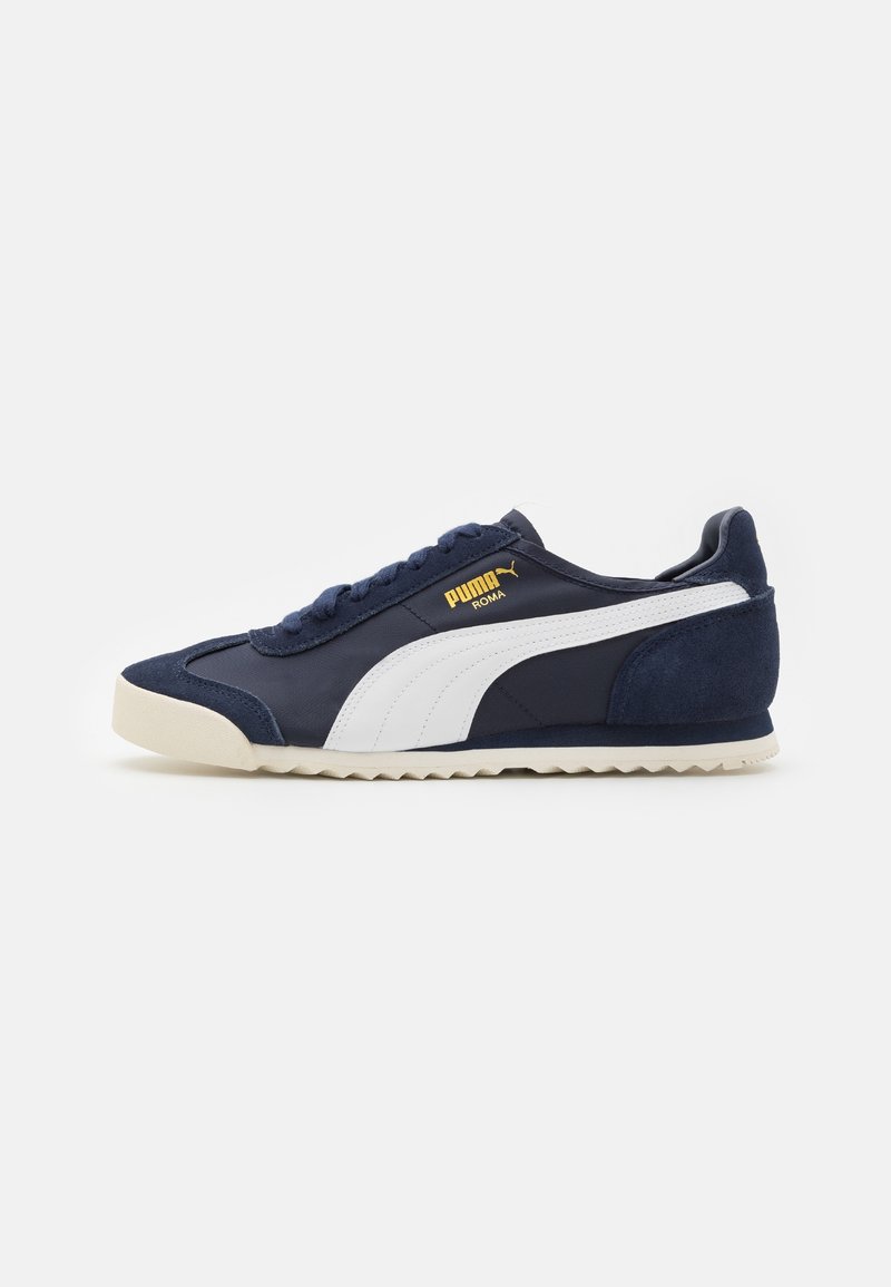 Zapatillas azul marino con una franja blanca, acentos de ante en la parte trasera y una suela de goma texturizada. Detalle del logo en dorado en el costado.