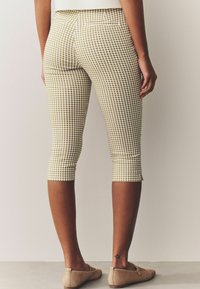 Bomulds capri-bukser i et lyst brun og hvidt ternet mønster, med en baglomme og cropped kant. Kombineret med beige fodtøj.