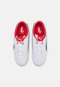 Scarpe sportive bianche con una superficie testurizzata, fodera interna rossa, dettagli neri e lacci bianchi. Logo Puma sulla linguetta e sul lato.
