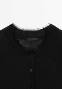 Cardigan noir boutonné avec un col rond présentant des bords effilochés et une étiquette de marque visible à l'intérieur du col.