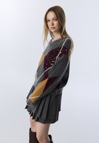 Grauer Mohair-Mix-Pullover mit einem Argyle-Muster in Braun, Senfgelb und Kastanienbraun. Merkmale sind eine entspannte Silhouette und weite, leicht verkürzte Ärmel.