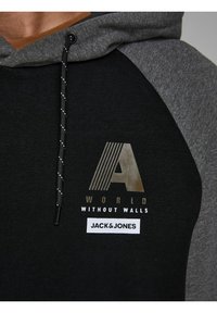 Primo piano di una felpa nera e grigia con la striscia "A", il testo "WORLD WITHOUT WALLS" e il logo del marchio "JACK & JONES" sul petto.