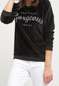 Sudadera de velour negra con mangas largas, con texto en gris contrastante que dice "HOY TE VES HERMOSA". Con puños y dobladillo acanalados.