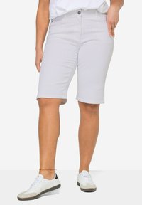 Shorts de Bermuda gris clair en tissu doux, avec une coupe slim, une fermeture à boutons et deux poches latérales. Associés à des baskets blanches.