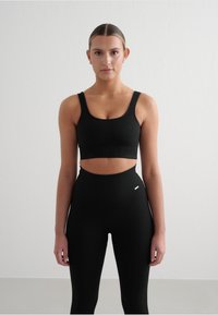 Schwarzer gerippter Sport-BH und hoch geschnittene Leggings mit Ausschnitt-Design. Weicher Stoff mit minimalem Hardware-Akzent an der Leggings.