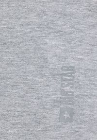 Helehall kangas õrna vertikaalse "FJG STAR" logoga ja tähega, mis on trükitud veidi tumedama halli tooniga.