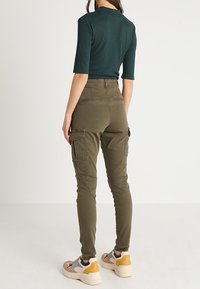 Pantalon cargo vert olive à coupe slim, avec poches latérales et passants pour ceinture, assorti à un haut ajusté vert foncé et des baskets multicolores.