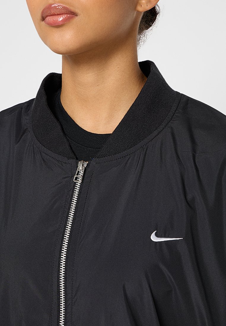 Czarna kurtka bomberka z zamkiem na przodzie, okrągłym kołnierzem i logo Nike. Wykonana z lekkiej, gładkiej tkaniny z ściągaczami na mankietach.