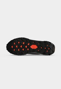 Semelle de chaussure noire et orange avec des crampons profonds et un petit logo au centre, conçue pour une utilisation en extérieur ou sur les sentiers.