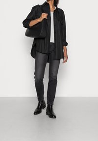 Czarna, oversize koszula z guzikami noszona na szarej koszulce, zestawiona z ciemnymi dżinsami i czarnymi botkami za kostkę. Niesiona jest fakturowana czarna torebka.