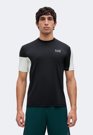 Homme portant un maillot de sport noir à manches courtes avec des panneaux blancs sur les manches et le logo EA7 Emporio Armani sur la poitrine.
