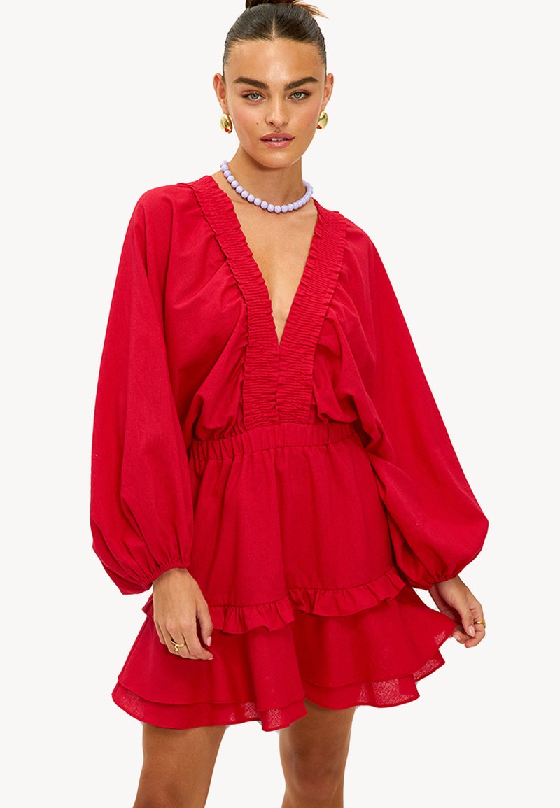 Robe rouge avec un décolleté en V profond, détail en ondulations texturé, longues manches bouffantes, et une jupe superposée avec des ourlets froncés.