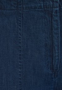Temno modra denim tkanina, ki se ponaša z gladko teksturo, navpičnimi šivi in subtilnim sijajem. Vključuje detajl zadnjega žepa.