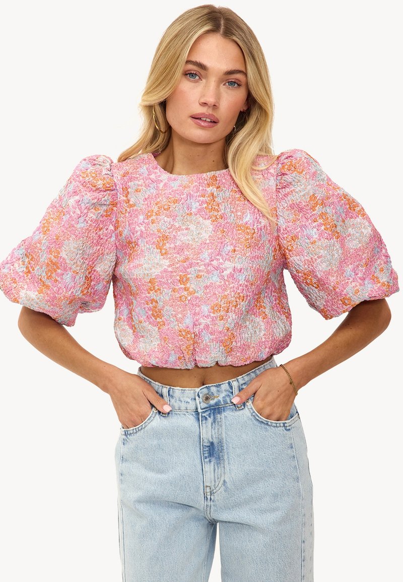 Haut court floral rose avec des manches bouffantes, un tissu texturé et un ourlet froncé, associé à un jean taille haute bleu clair.