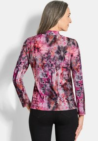 Langsleeve, aansluitend top gemaakt van lichte stof met een levendig roze en paarse abstracte patroon met bloemdetails.