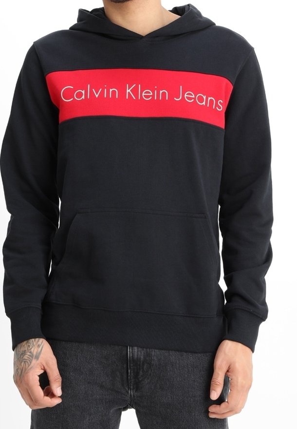 Sudadera negra con una franja roja horizontal que presenta el texto "Calvin Klein Jeans". El material parece suave, con un bolsillo frontal y capucha ajustable.
