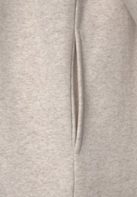 Tejido de sudadera gris claro con un acabado suave y texturizado y aberturas para los bolsillos laterales. Los detalles de las costuras son sutilmente visibles a lo largo de los bordes.
