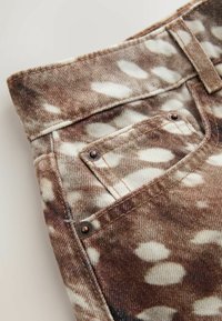 Gros plan d'un jean en denim marron et blanc à motif tie-dye avec une poche avant visible et des rivets métalliques.