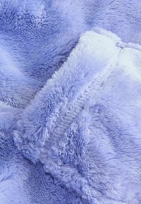Weiches, flauschiges Material in einem helllila Farbton, das Texturen und Nähte zeigt und ein gemütliches und einladendes Erscheinungsbild schafft.